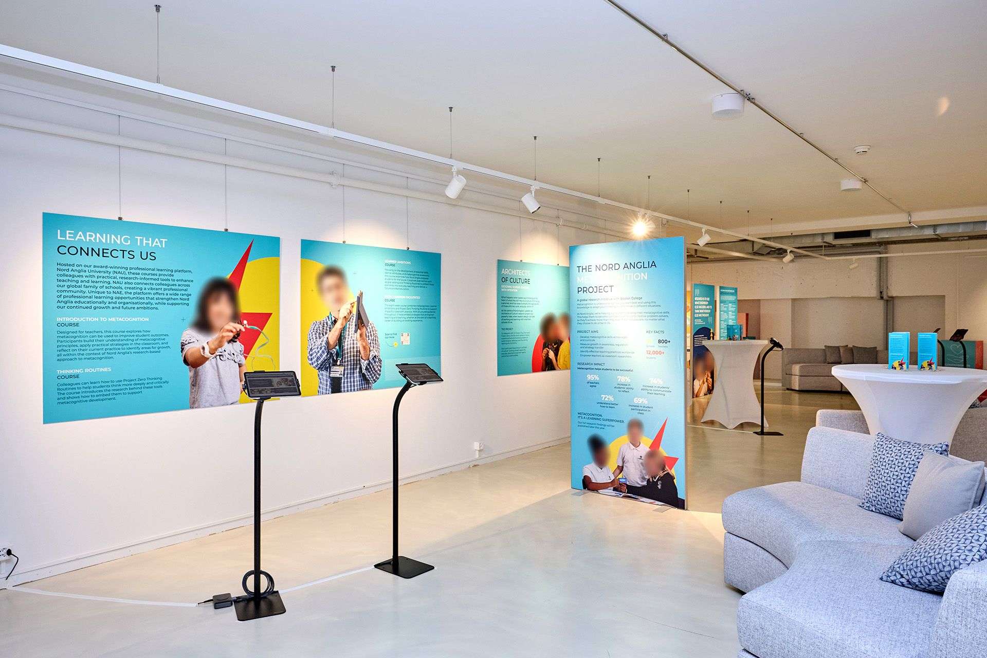 A large room with hanging display boards against the walls and free standing, a sofa, podiums and tables