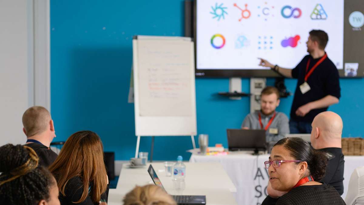 Our creative director Tom Walton pointing at a screen of company logos in front of an audience during a workshop